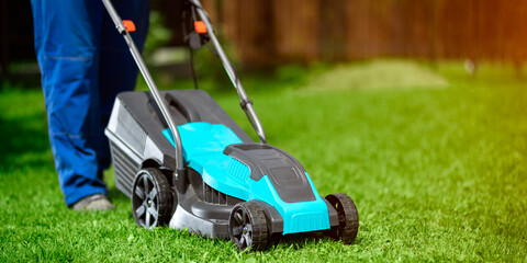 Lawn grass mowing. Worker cutting grass in a green yard. A man with an electric lawn mower mowing a...