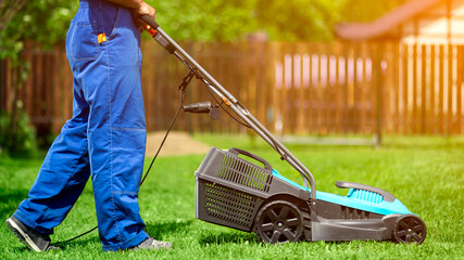 A man with an electric lawn mower mowing the lawn.Adult man pruning and landscaping a garden,...