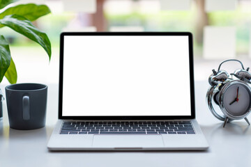 Fototapeta premium Laptop blank white screen with clock coffee mug placed on table. Mock up.