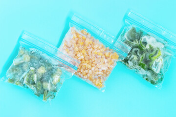 Three packages with frozen vegetables on blue background, top view.