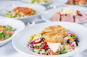 A view of several salad plates, featuring a breaded chicken antipasto salad.