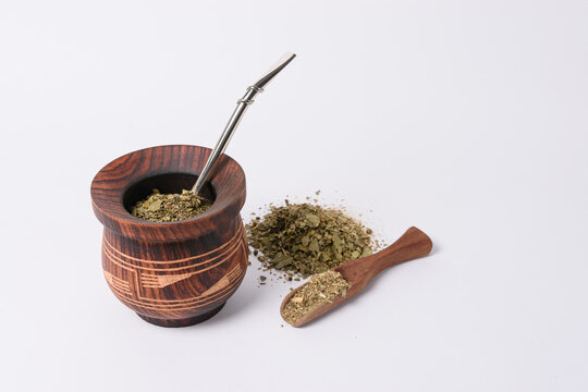 Mate con bombilla cebado con yerba mate y cuchara de madera sobre fondo blanco 