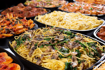 A view of several varieties of pasta trays, featuring a tray of mushroom and spinach spaghetti.