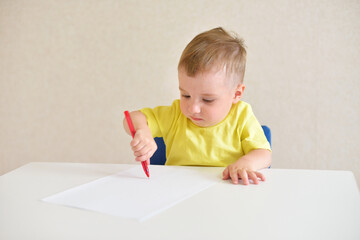 toddler boy plays draws on a piece of paper with a red pen sitting at a white table. educational game Montessori fine motor skills. early development concept.