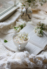 Fresh Spring blossom with a cup of coffee near window with raindrops where sheer curtain and string lights are hanging