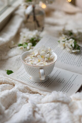 Fresh Spring blossom with a cup of coffee near window with raindrops where sheer curtain and string lights are hanging