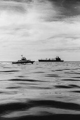 Two fishing boats in the sea in the horizon and cloudy sky (in black and white)