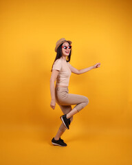 Fototapeta na wymiar Beautiful young south east Asian woman red frame sunglass hat pose act walk move forward on yellow orange background