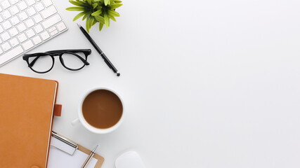 Top view white wooden workspace office desk with computer and office supplies. Flat lay work table with blank notebook, keyboard, green leaf and coffee cup. Copy space for your advertising content.