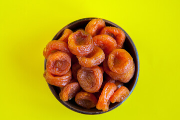 Dried orange dried apricots in a clay cup on a yellow background, top view