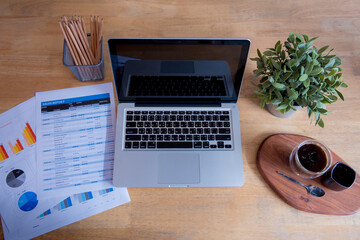 Office laptop business financial document chart and graph on wooden table with coffee cup. Flat lay...