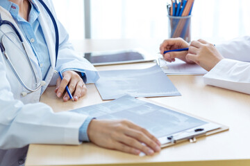 Two asian women doctors discuss meeting doctor's office medical clinic looking x-ray film consulting patient disease. Asian medical lab young women talking together discussing healthcare teamwork