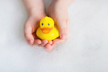 Little child holding yellow rubber duck in bubble bath. Baby hygiene, accessories for bathing,...