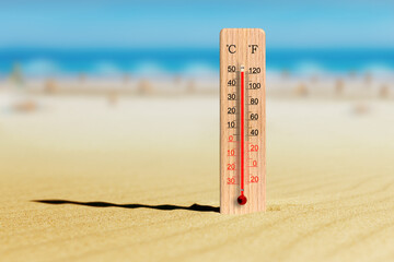 Sea coast at hot summer day. Wooden thermometer in the sand. Ambient temperature plus 50 degrees celsius