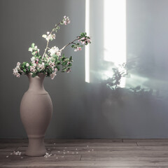 branches of  apple tree with flowers in  floor vase against  gray wall