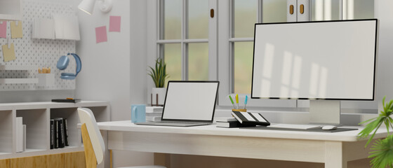 Computer and laptop with mock-up screen on the table beside the window in White concept study room, 3D rendering