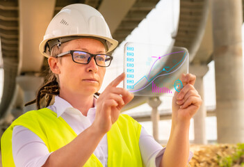 Female engineer or inspector at bridge construction site working on futuristic gadget analyzing data.