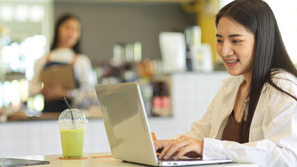 Female teenager smiling and using laptop while sitting in coffee shop