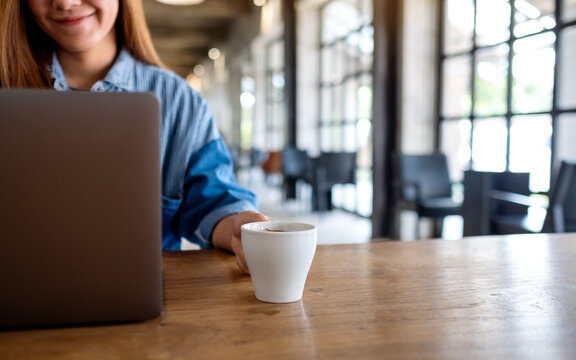 Closeup image of a young woman using and working on laptop computer while drinking coffee in cafe