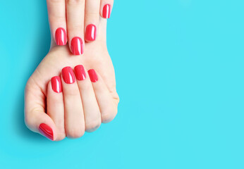 Female hands with red manicure on blue background, copy space - obrazy, fototapety, plakaty