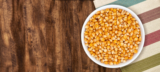 Top view of bowl with Popcorn Kernels Uncooked. Popcorn Kernels Uncooked in a Ceramic Bowl. The image is a cut out, isolated on a wood background, with a clipping path