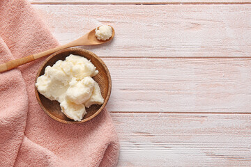 Bowl with shea butter on light wooden background