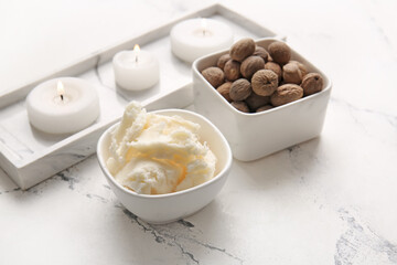 Bowls with shea butter, nuts and burning candles on light background