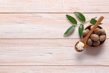 Spoon with shea butter and nuts on light wooden background