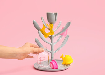 Female hand and drying rack for baby bottles on color background