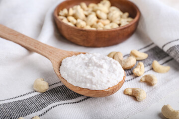 Spoon with sour cream and cashew nuts on light background, closeup