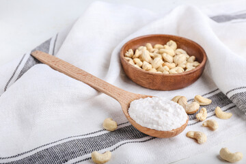 Spoon with sour cream and cashew nuts on light background
