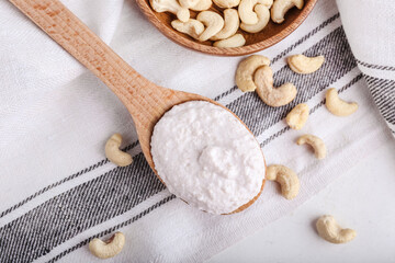 Spoon with sour cream and cashew nuts on light background, closeup