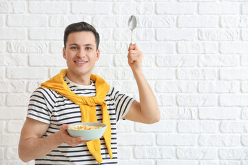 Young man and bowl with cornflakes on brick background