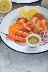 Asia Art Gravlax Graved Lachs, ein roh gebeizter Fisch mit Zitronengras und Chili auf Emaille Teller mit Hovmästarsås Senf Soße, Toast, Zwiebel Ringe, Dill, Zitrone und Leinen Tuch auf hell Marmor Hin