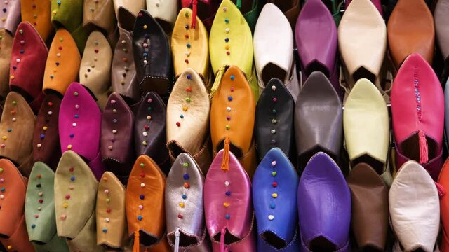 Authentic colorful Moroccan slippers (babouches), displayed on a wall, in the medina of Marrakech (Marrakesh), Morocco. Camera movement from left to right.