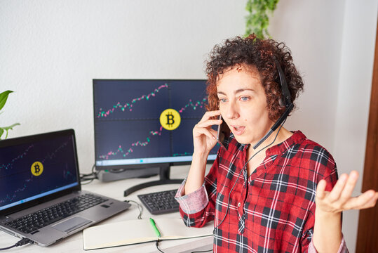 Shocked trader woman talks on the mobile phone with some screens with cryptocurrency data on her computer