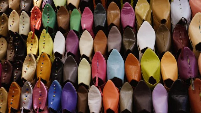 Authentic colorful Moroccan slippers (babouches), displayed on a wall, in the medina of Marrakech (Marrakesh), Morocco. Camera movement from right to left.