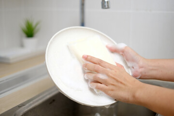 Woman's hand washing white dishes on the sink. Point of view POV plate washing with foam.