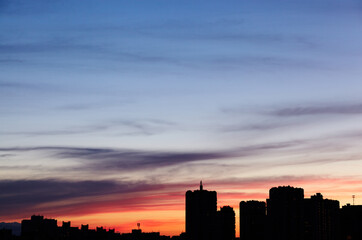 Colorful dramatic sky with clouds at sunset. City during warm sunset