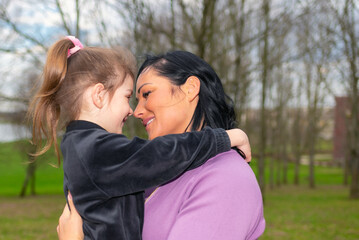 Fototapeta premium Beautiful mother and daughter play hugs in a spring park nature in profile looking at each other.