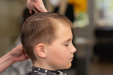 Cute little boy getting haircut by hairdresser at the barbershop.Side view.Closeup.