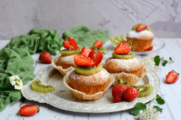 Homemade sweet cupcakes with strawberries and kiwi on a light gray wooden background, selective focus. The concept of a delicious and healthy breakfast