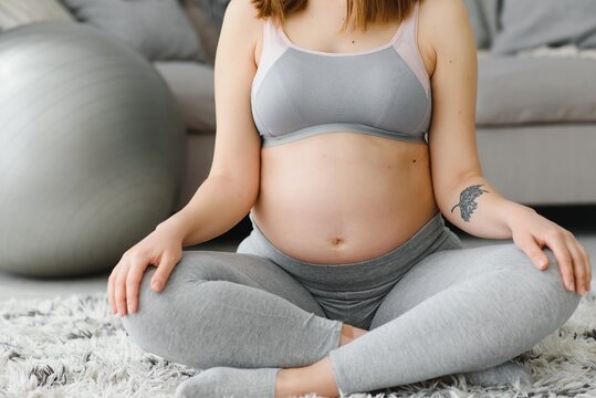 Closeup shot of unrecognizable pregnant woman meditating at home, expetcant lady sitting in lotus position with clasped hands, practicing yoga for healthy pregnancy, cropped image with free space