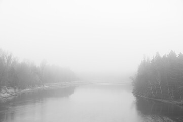 Fototapeta premium River surrounded by forest during fog. Minimal composition, monochrome image. Place for text