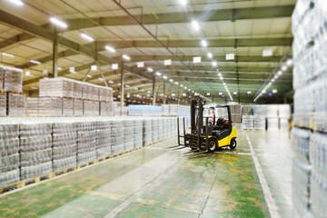 Yellow loader on the background of a huge industrial food warehouse with plastic PET bottles with beer,  water,  drinks.