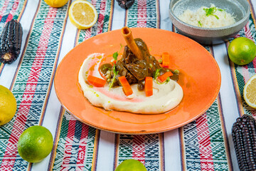 Stewed lamb shank with mashed potatoes and vegetables in orange plate on the colorful peruvian tablecloth