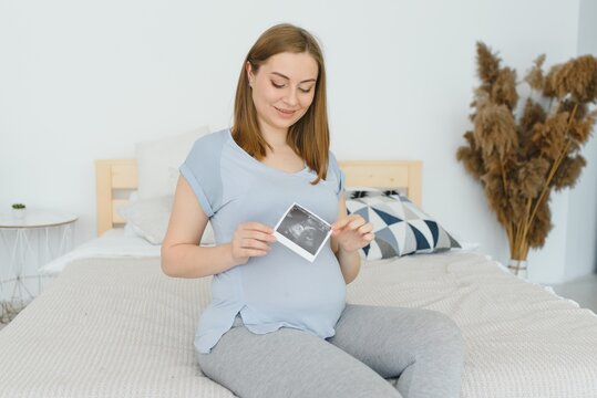 Pregnant woman looking at her baby sonography. Happy expectant lady enjoying first photo of her unborn child, anticipating her future life, copy space