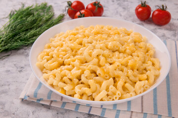 Macaroni and cheese on a white plate with parsley and cherry tomatoes on a gray background
