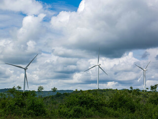 Wind turbines on the green hilly terrain with the bright blue sky.
