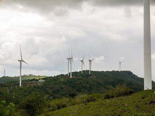 Wind turbines on the green hilly terrain with the bright blue sky.